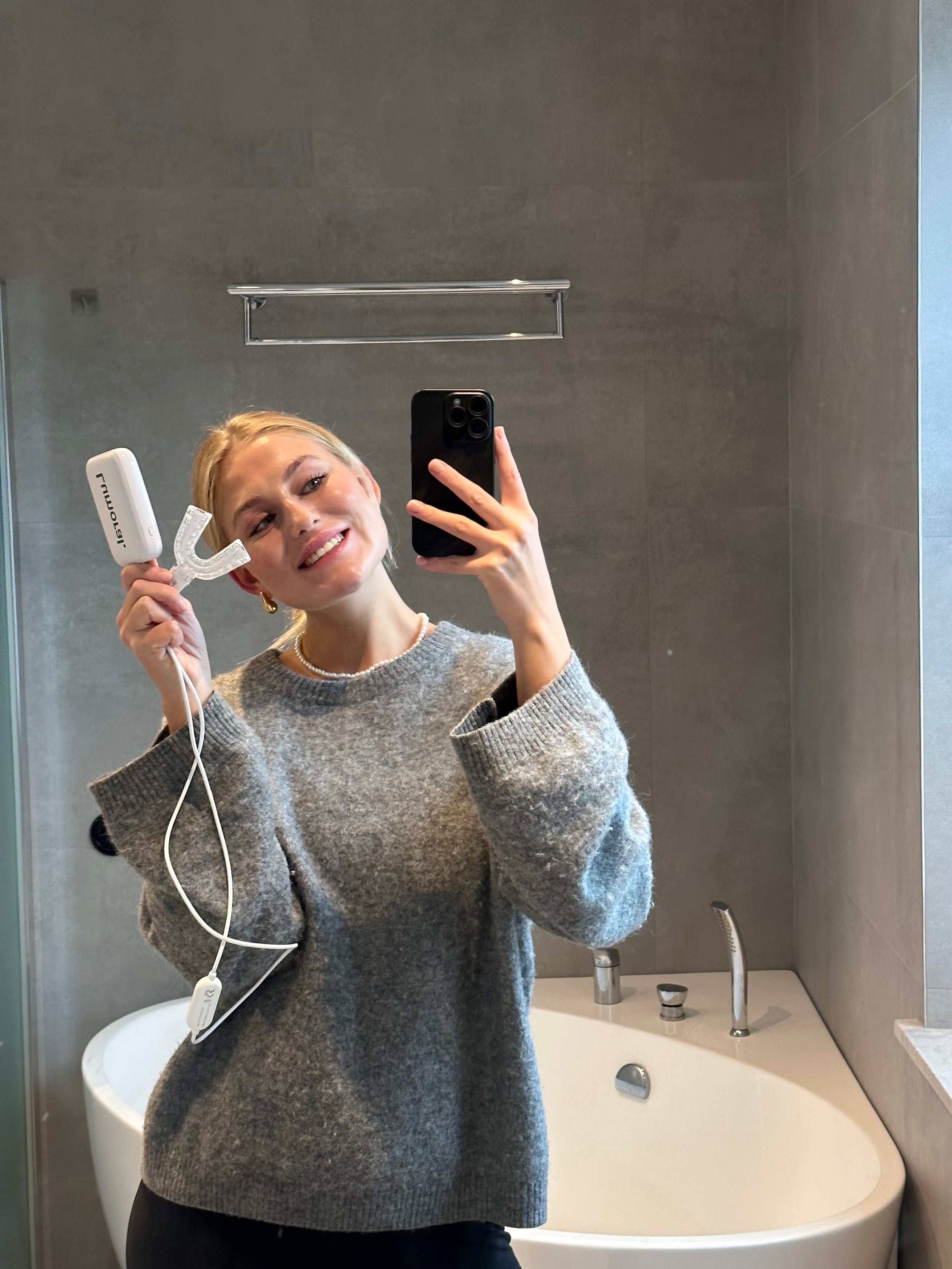 Jonge vrouw neemt spiegelselfie met Lumoral mondstuk in de hand aangesloten op externe batterij