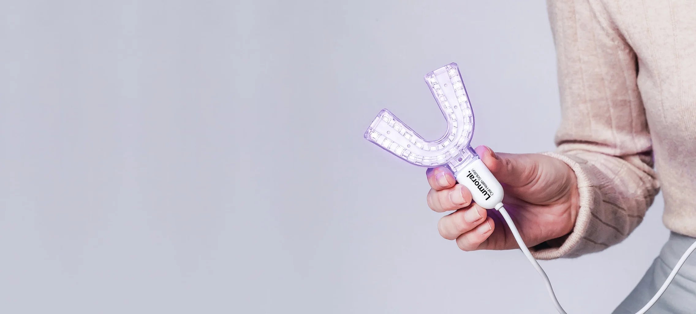 Een close up van het lumoral mondstuk dat iemand vast heeft in haar hand met oplaadkabel erbij