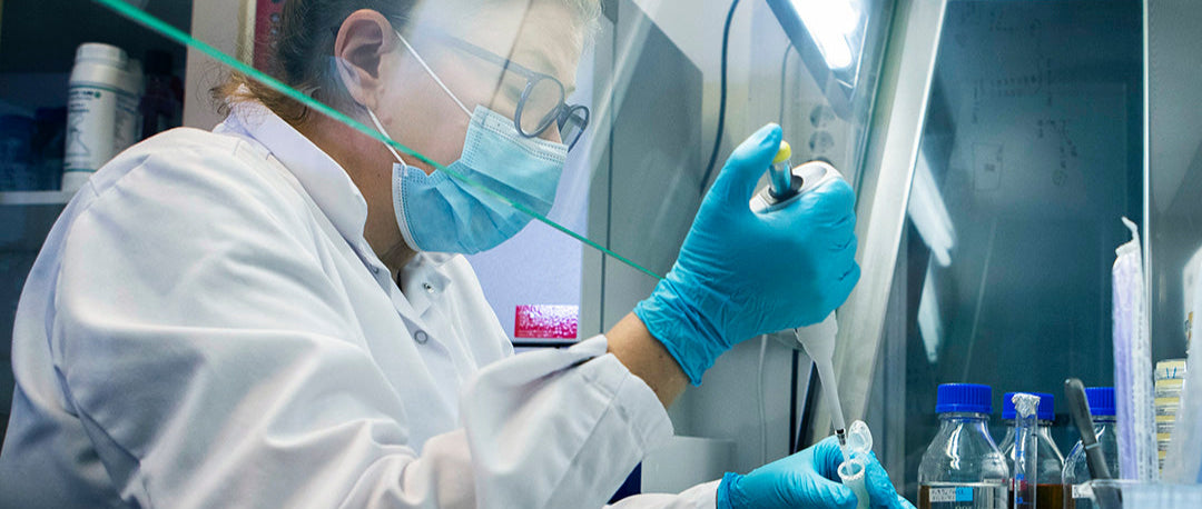 vrouw met mondmasker en handschoenen is met een pipet aan het werken in een labaratorium.