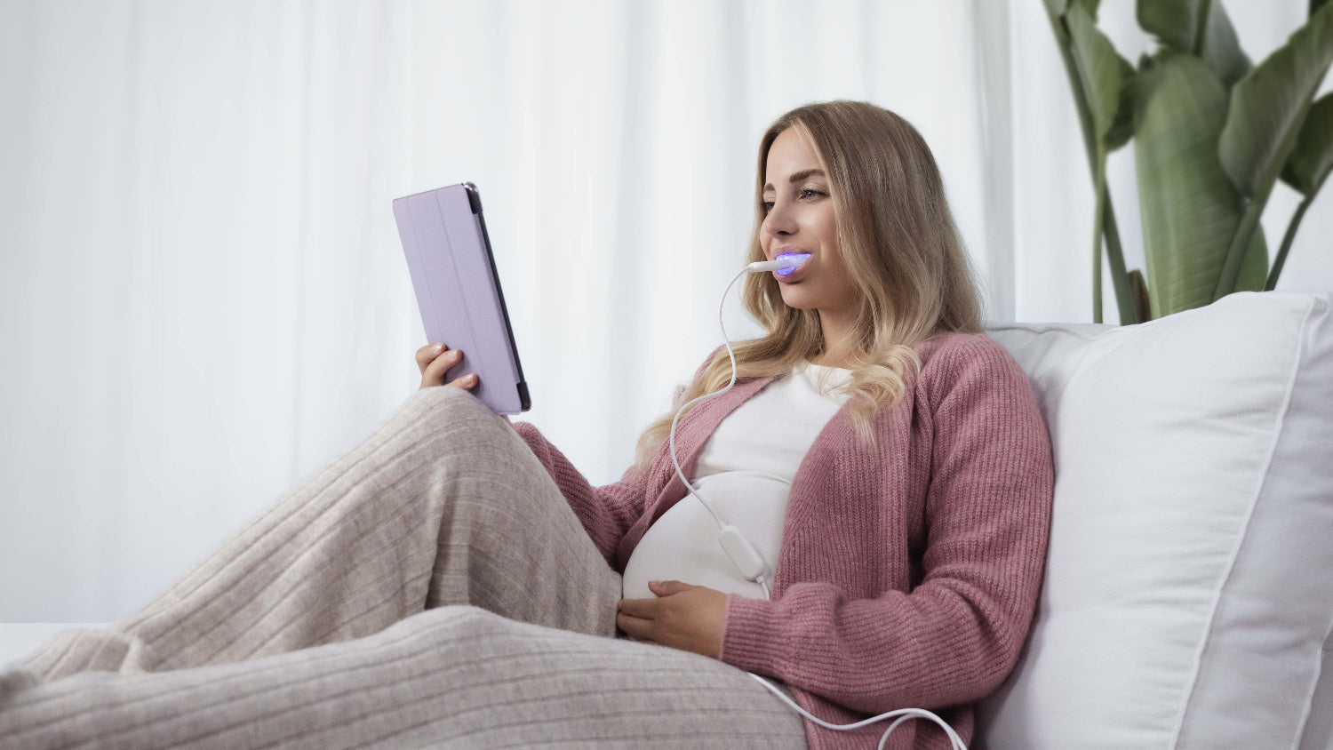 Een zwangere vrouw die het lumoral mondstuk in haar mond heeft terwijl ze rustig in de zetel op haar ipad werkt.